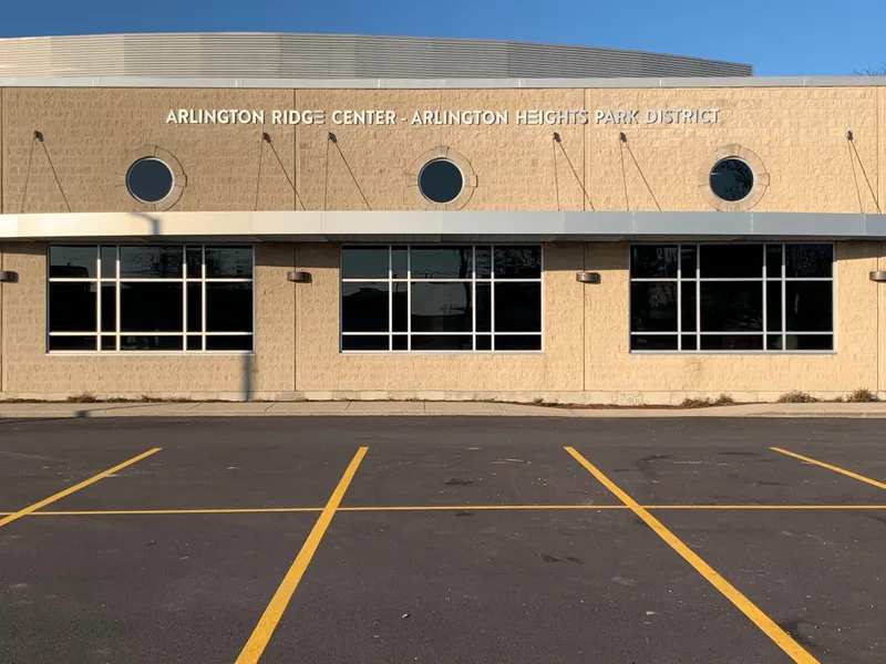 Arlington Ridge Center exterior — clean dimensional metal letters across a tan-brick recreation facility under blue sky.