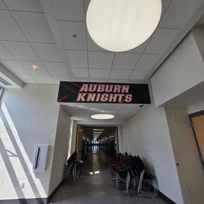 Auburn High School hallway — large 'AUBURN KNIGHTS' suspended banner panel with red & white block lettering on a black background, mounted in the corridor between classrooms.