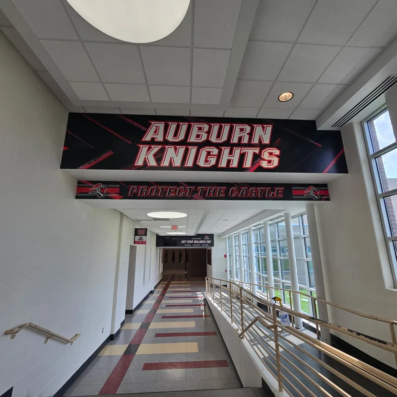 Auburn High School corridor — suspended "AUBURN KNIGHTS / Protect the Castle" header panels spanning a long sunlit hallway.