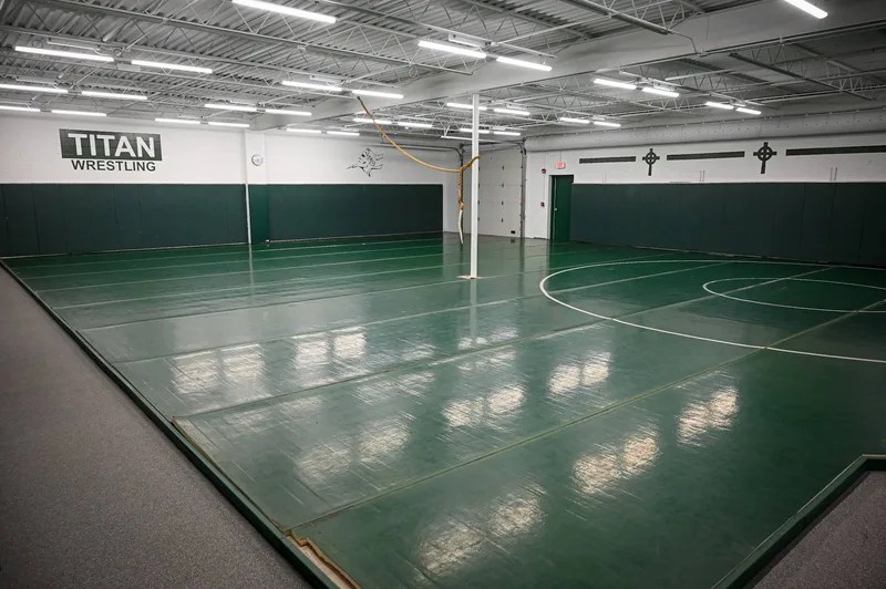 Boylan Catholic High School wrestling room — "TITAN WRESTLING" wall graphic, Titan helmet logo and cross icons above green wall pads and a full-room mat.