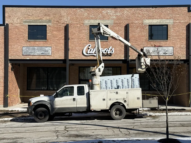 CorPro bucket truck staged at the curb while installers mount the dimensional "Cahoots" script on the historic brick facade.