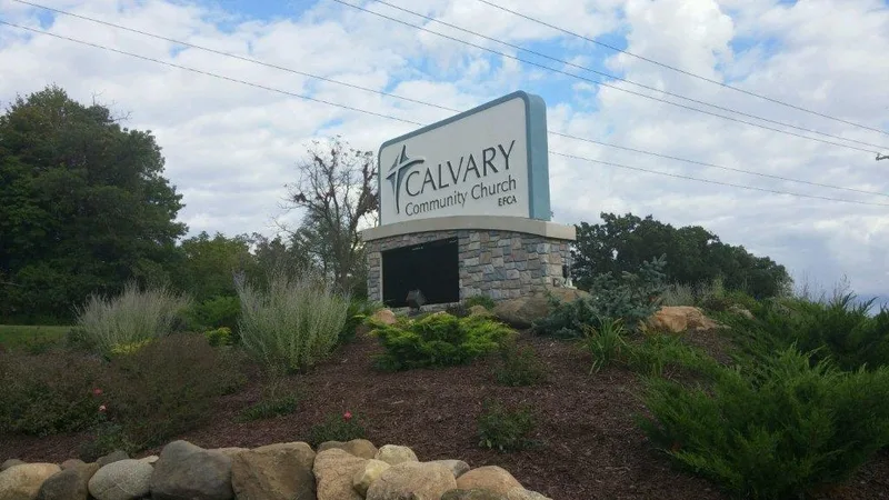 Calvary Community Church entrance monument — large arched cabinet with star-cross logo over a stone-clad base, surrounded by a landscaped berm with shrubs and boulders.