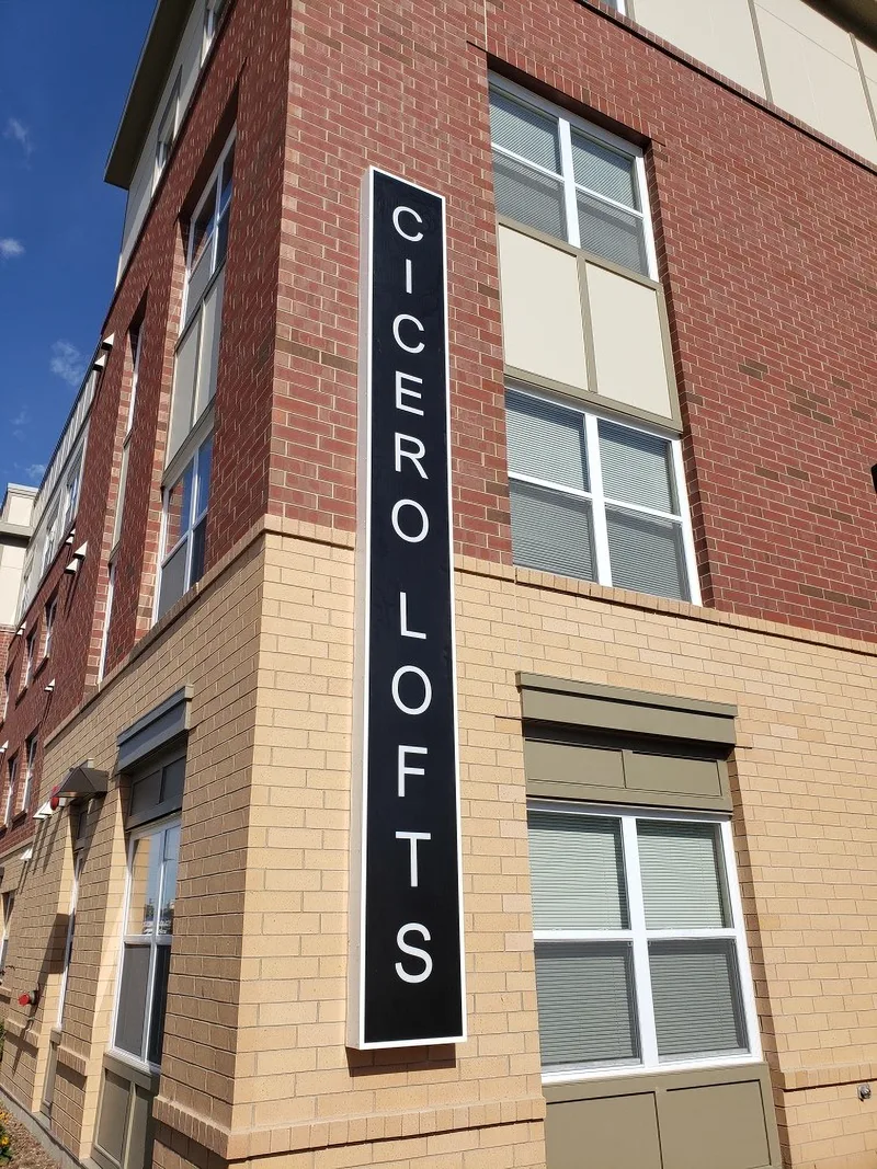 Vertical exterior building sign for Cicero Lofts — tall black panel with stacked white lettering mounted on a brick facade corner.