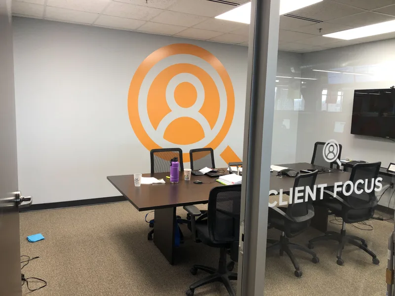 Comply365 Client Focus conference room — orange person-with-target wall graphic and frosted-glass "CLIENT FOCUS" door inscription.