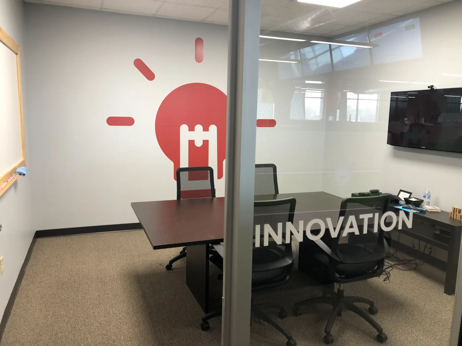 Comply365 Innovation conference room — red lightbulb wall graphic and frosted-glass "INNOVATION" door inscription.