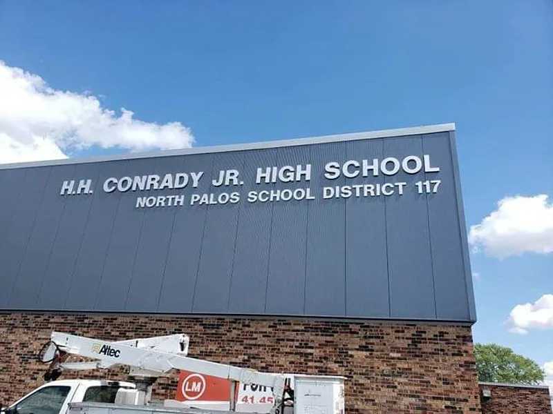 H.H. Conrady Jr. High School building ID — large dimensional letters mounted on a metal panel above the brick facade, with a CorPro install lift in frame.
