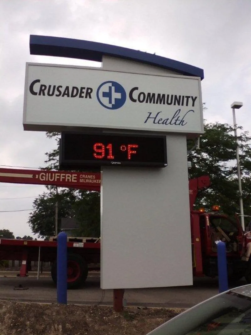 Crusader Community Health monument pylon with LED temperature display reading 91°F, set against a Giuffre install crane in frame.