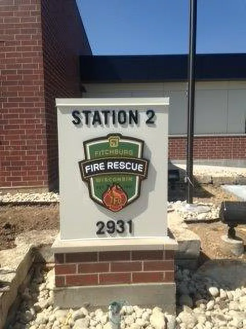 Fitchburg Fire Rescue Station 2 entry monument — full-color cast dimensional shield mounted on a stucco and brick base.