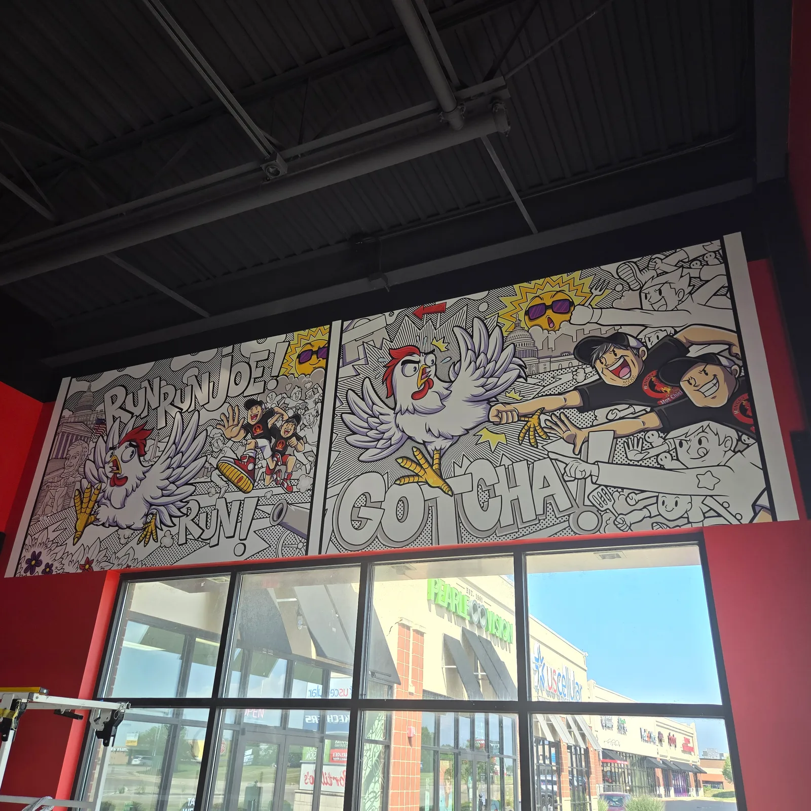 Hangry Joe's Hot Chicken Rockford interior mural — vibrant comic-book panels reading 'RUN RUN JOE! RUN!' and 'GOTCHA!' featuring the chicken mascot in dramatic action poses, installed across the dining room wall above the storefront windows.