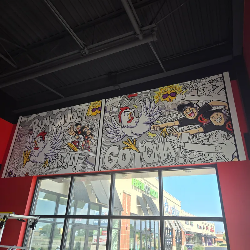Hangry Joe's Hot Chicken Rockford interior mural — vibrant comic-book panels reading 'RUN RUN JOE! RUN!' and 'GOTCHA!' featuring the chicken mascot in dramatic action poses, installed across the dining room wall above the storefront windows.