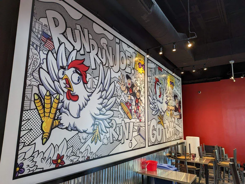 Hangry Joe's San Marcos, TX dining room — black-and-white comic-book mural panels ("RUN RUN JOE! RUN!", "GOTCHA!") with the red-combed rooster mascot, set against a red accent wall.