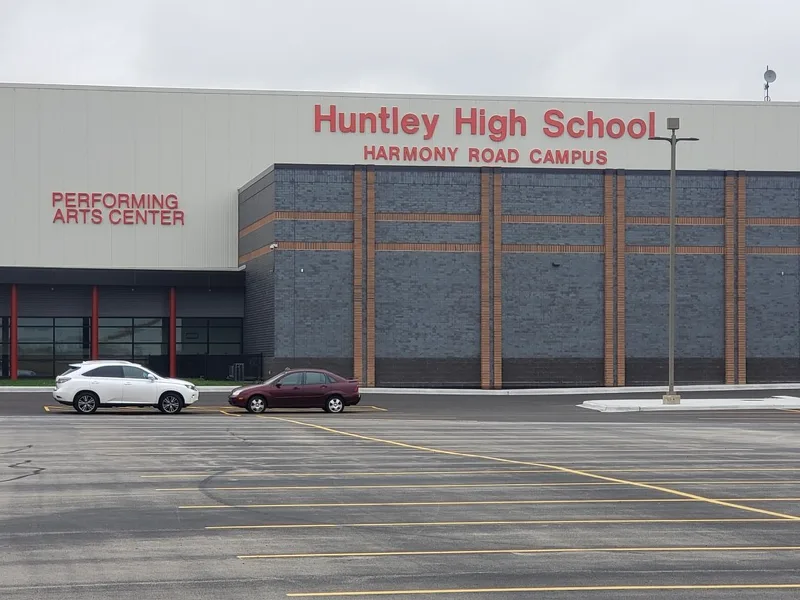 Huntley High School Harmony Road Campus — red dimensional letters across the upper facade with a separate "PERFORMING ARTS CENTER" ID on the gray block wall.
