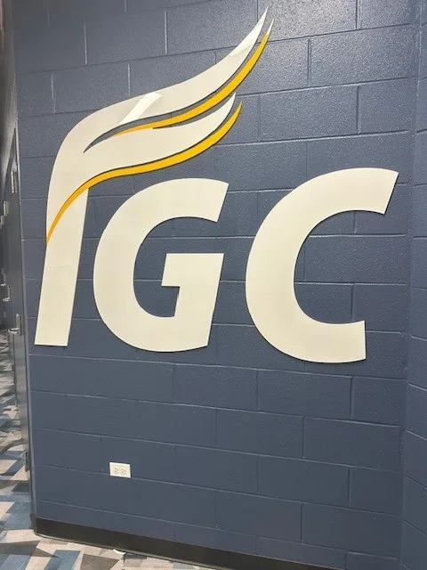IGC oversized dimensional wall logo — white-and-gold "IGC" with stylized flame mounted across a navy cinder-block wall.