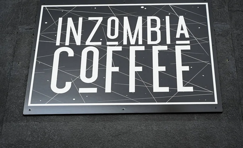 Inzombia Coffee sign — black panel with white routed "INZOMBIA COFFEE" lettering and a fine geometric line pattern framed by a white border.