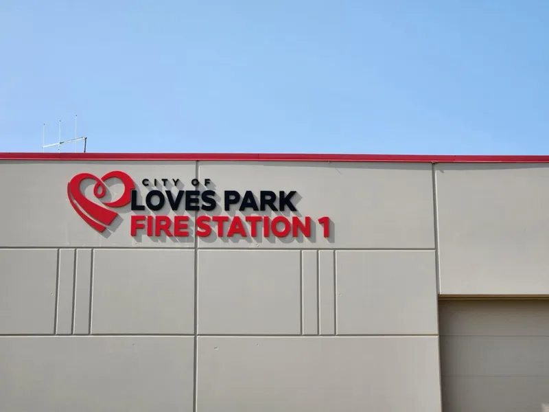 City of Loves Park Fire Station 1 building ID — red and black dimensional letters with heart-and-flame logo mounted on a cream paneled facade.