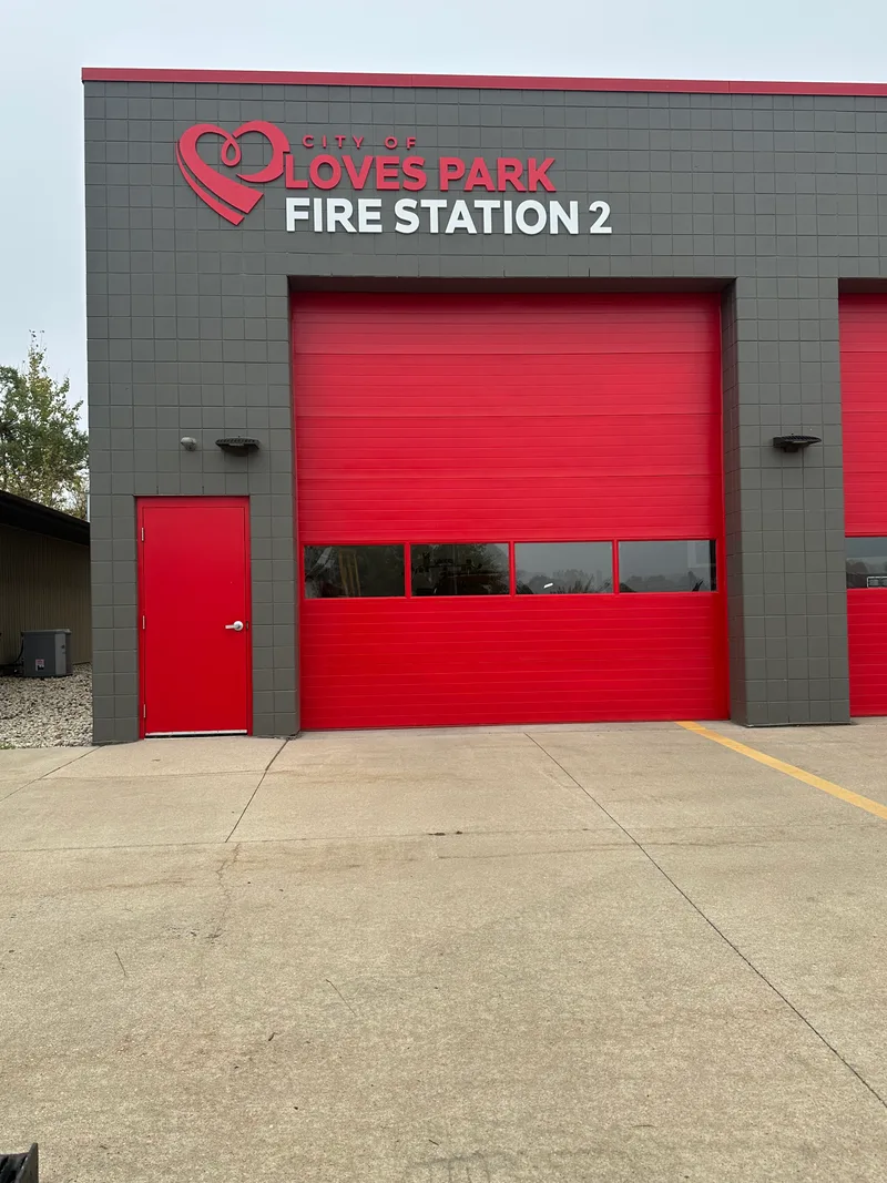 City of Loves Park Fire Station 2 — red and gray facade with dimensional 'CITY OF LOVES PARK FIRE STATION 2' lettering and the LP heart-flame logo over the apparatus bays.