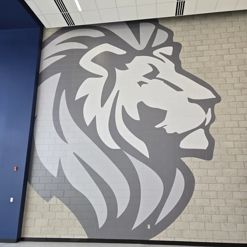 Lyons Township High School — oversized two-tone gray lion-head mascot graphic applied across a full-height block wall beside a navy accent column.