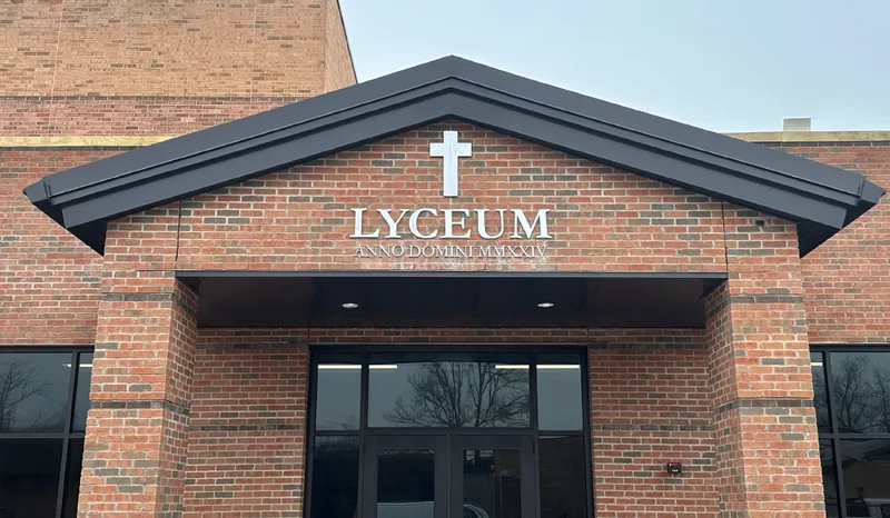 Lyceum Church entrance — brushed-metal dimensional 'LYCEUM' lettering and a cross emblem mounted on the brick gable above the glass entry, with 'ANNO DOMINI MMXXIV' inscription below.