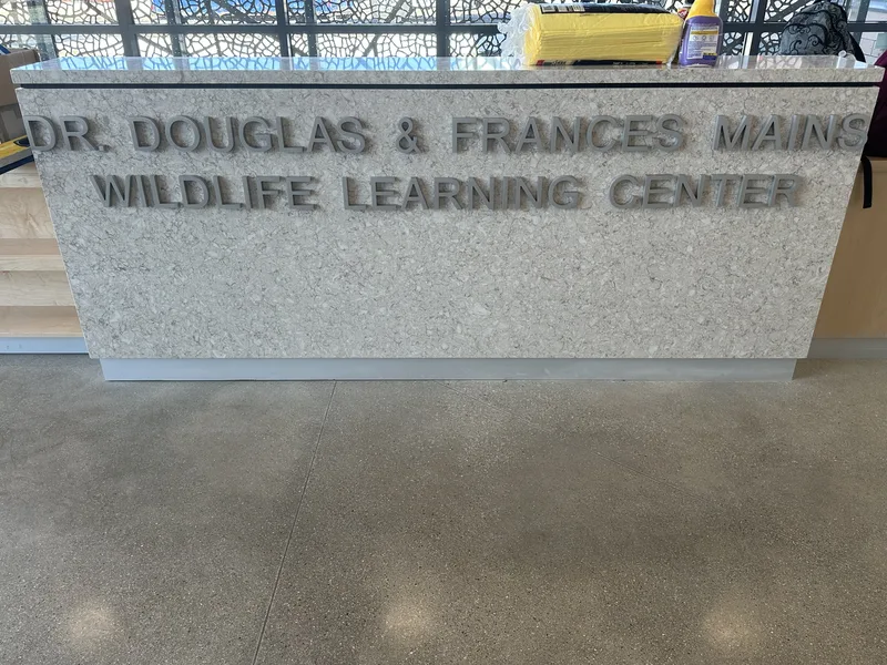 Brushed-metal dimensional letters reading "DR. DOUGLAS & FRANCES MAINS WILDLIFE LEARNING CENTER" mounted on a terrazzo-style reception counter.