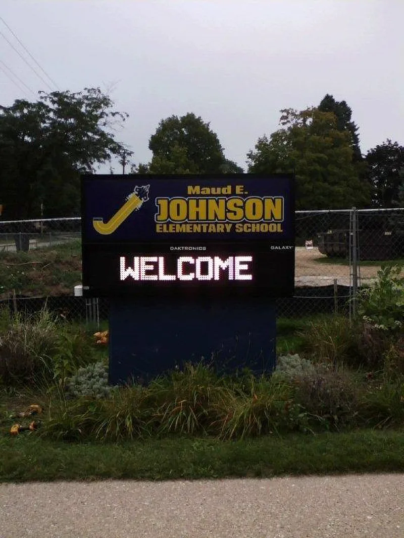 Maud E. Johnson Elementary School monument — navy cabinet with gold school name over an LED message board reading "WELCOME", in a planted bed.