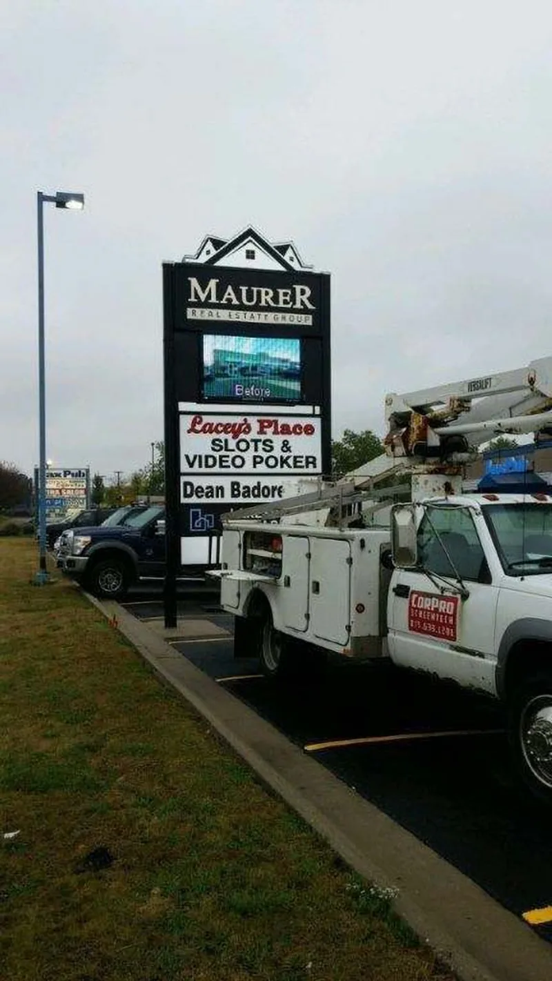 Completed Maurer Real Estate Group pylon sign — multi-tenant cabinet with LED message screen and CorPro bucket truck parked alongside, mid-final-inspection.