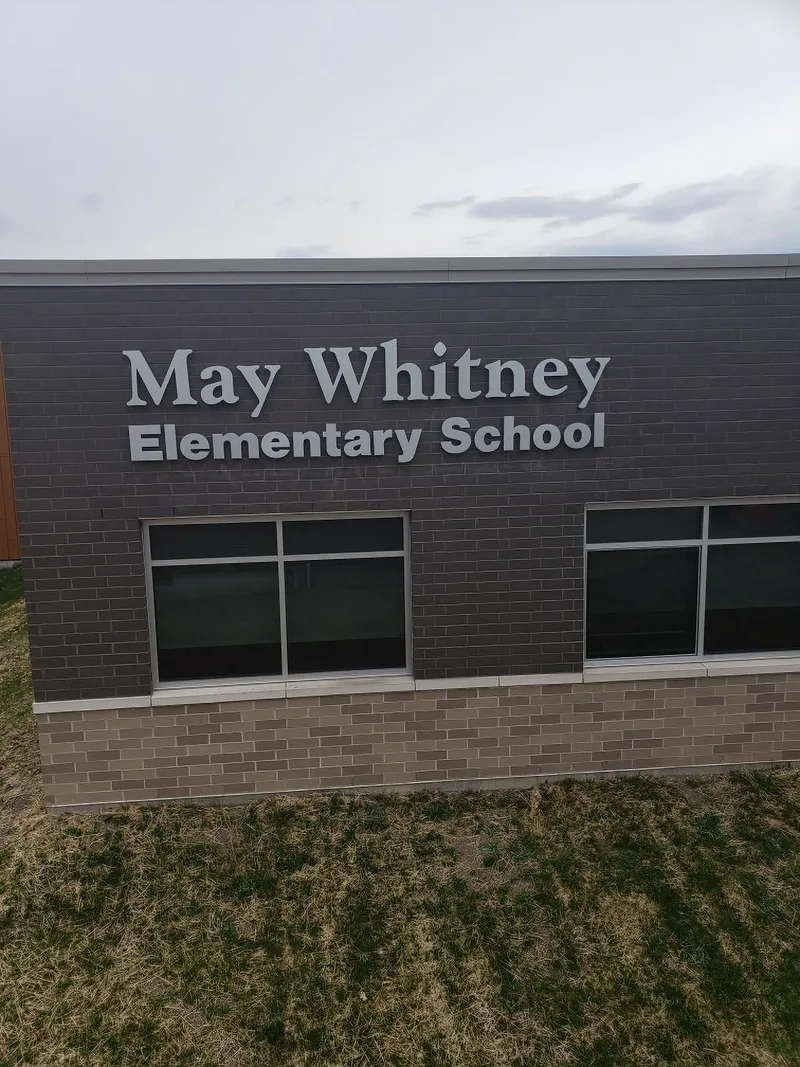 May Whitney Elementary School — brushed-aluminum dimensional letters on a dark brick facade above a row of classroom windows.