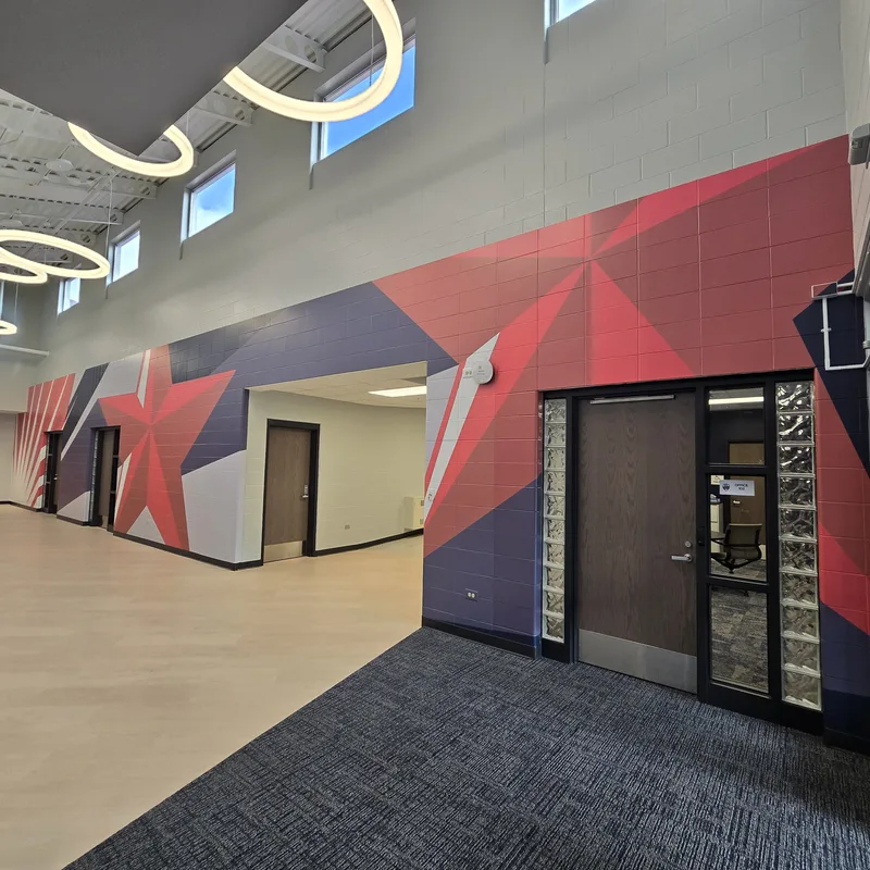 Nathan Hale Primary School commons — two-story geometric red, white and navy star mural wrapping the corridor walls beneath clerestory windows and ring pendant lights.