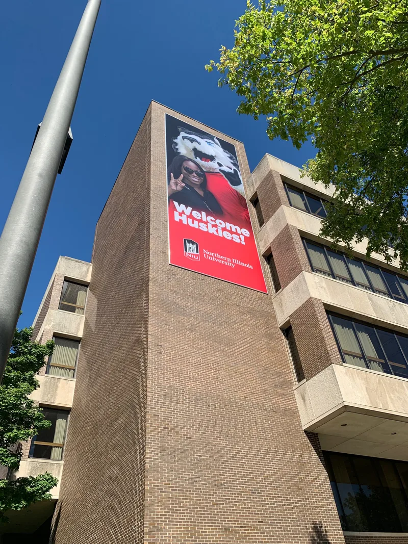 Tall red "Welcome Huskies!" banner with the NIU Huskie mascot, mounted high on a brick tower at Northern Illinois University.