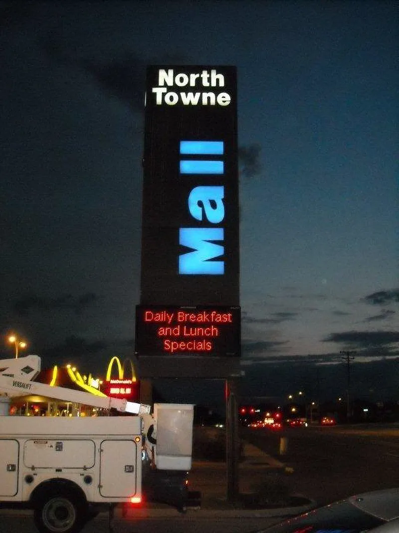 North Towne Mall pylon at dusk — illuminated "North Towne" header and glowing blue vertical "Mall" letters over a red LED message center, CorPro bucket truck in the foreground.