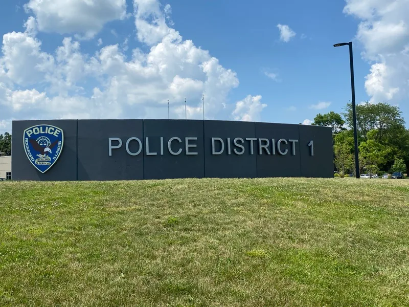 Police District 1 exterior monument wall — dark cladding with large dimensional "POLICE DISTRICT 1" letters and a full-color department shield.