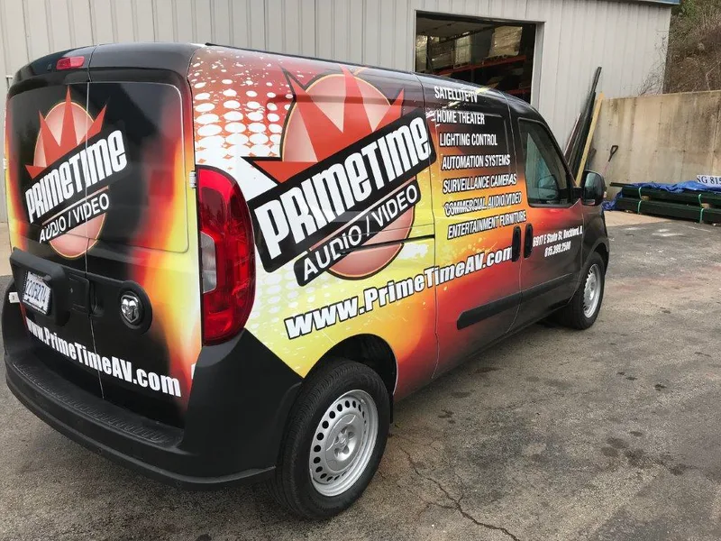 PrimeTime Audio/Video compact van — rear three-quarter full wrap with flame gradient, logo and www.PrimeTimeAV.com across the rear doors.