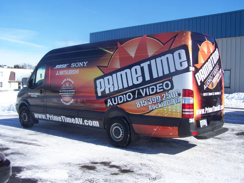 PrimeTime Audio/Video Sprinter van — full wrap with fiery orange starburst, "PRIMETIME AUDIO/VIDEO" logo, brand partners and website, parked in snow.