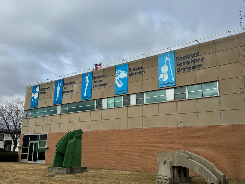 Riverfront Museum Park, Rockford — exterior banner panels for Discovery Center, Rockford Art Museum, Rockford Dance Company, Burpee Museum, and Rockford Symphony Orchestra mounted along the upper facade beside an American flag.