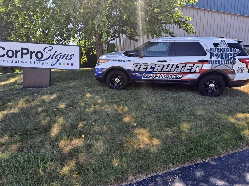 Rockford Police Recruiting Explorer — red, white and blue patriotic wrap with "RECRUITER" and phone number, parked beside the CorPro Signs monument.