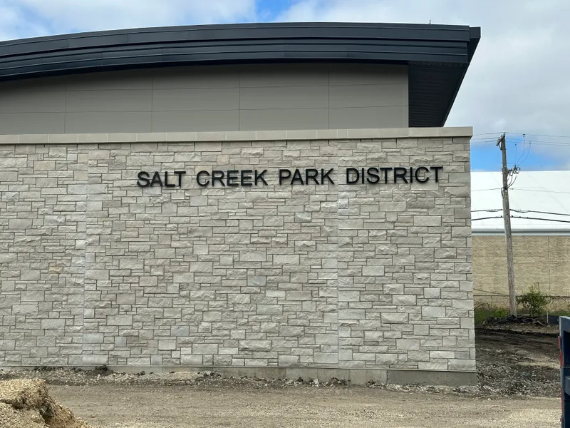 Salt Creek Park District building identification — black dimensional letters mounted to a stone-veneer exterior wall under a contemporary curved metal roofline.