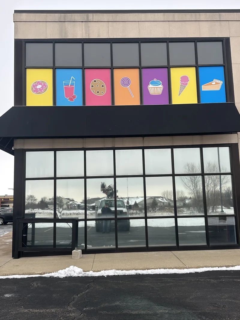 Sugar Jones storefront — row of bright clerestory window panels with donut, drink, cookie, lollipop, cupcake, ice-cream and pie icons above the black awning.