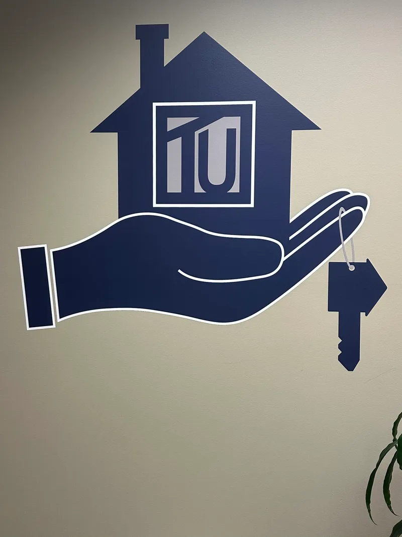 Title Underwriters office wall graphic — dimensional navy-blue cut vinyl of a hand cradling a house with 'TU' window emblem and a house-shaped key tag, installed as the lobby brand feature.
