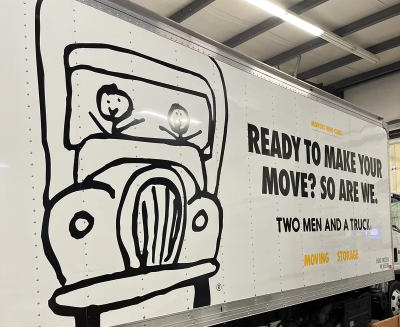 Two Men and a Truck box-truck side — signature stick-figure truck drawing and "READY TO MAKE YOUR MOVE? SO ARE WE." headline, installed in the CorPro shop.