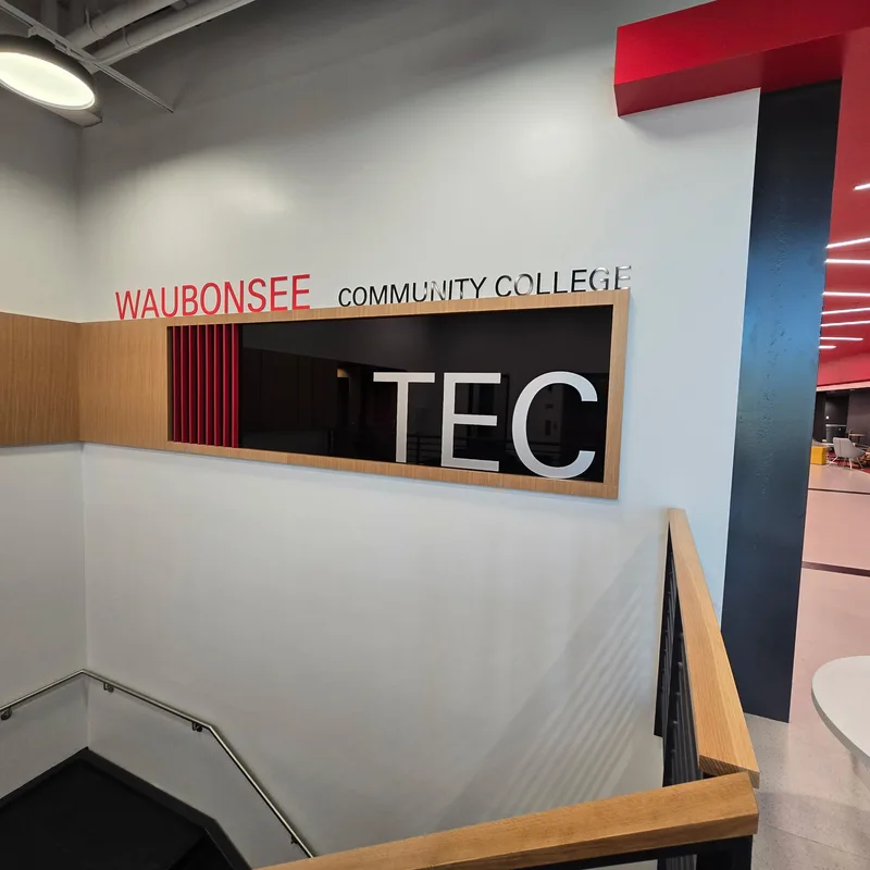 Waubonsee Community College Technical Education Center — red and gray "WAUBONSEE COMMUNITY COLLEGE" lettering with a large dimensional "TEC" over the stairwell overlook.