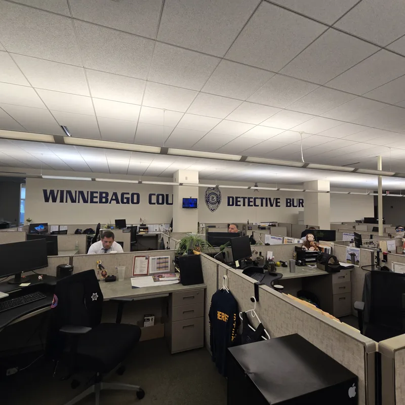 Winnebago County Detective Bureau office — full-length navy "WINNEBAGO COUNTY DETECTIVE BUREAU" wall graphic with badge running above the cubicles.