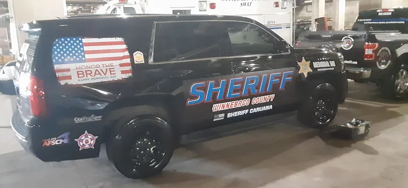 Black Sheriff Tahoe with chrome-blue "SHERIFF Winnebago County" lettering and an American-flag "Honor the Brave" rear-window graphic.