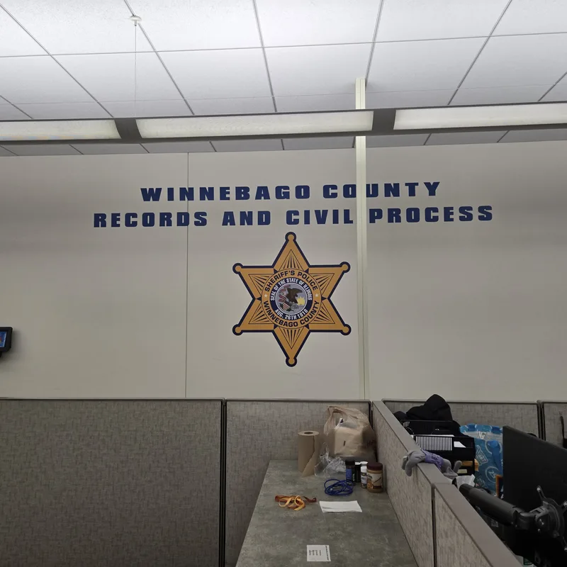 "WINNEBAGO COUNTY RECORDS AND CIVIL PROCESS" navy wall lettering above a full-color Sheriff's star in the records office.