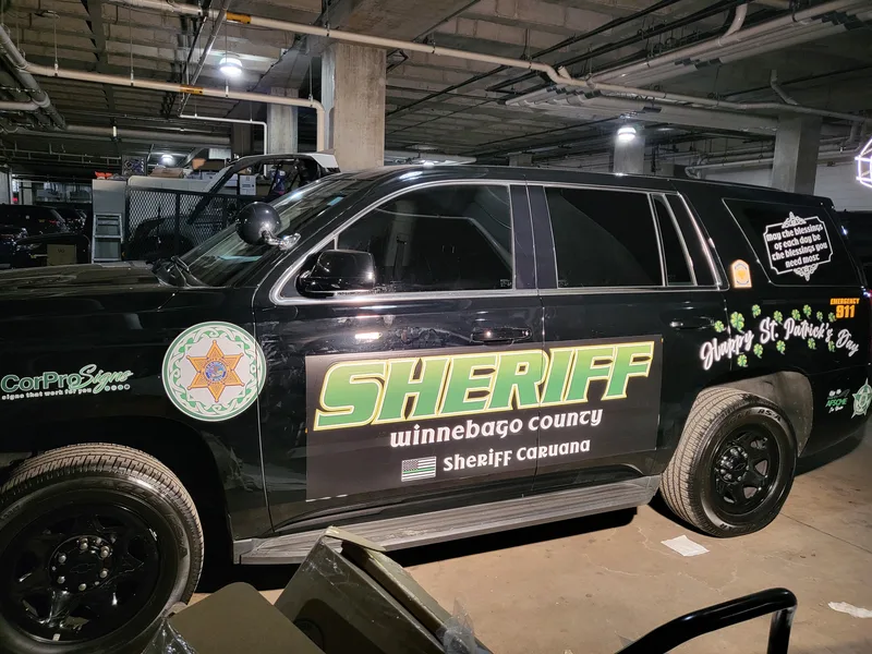 Seasonal Sheriff Tahoe — lime-green "SHERIFF Winnebago County" door graphic with shamrocks and "Happy St. Patrick's Day" lettering on a black SUV.