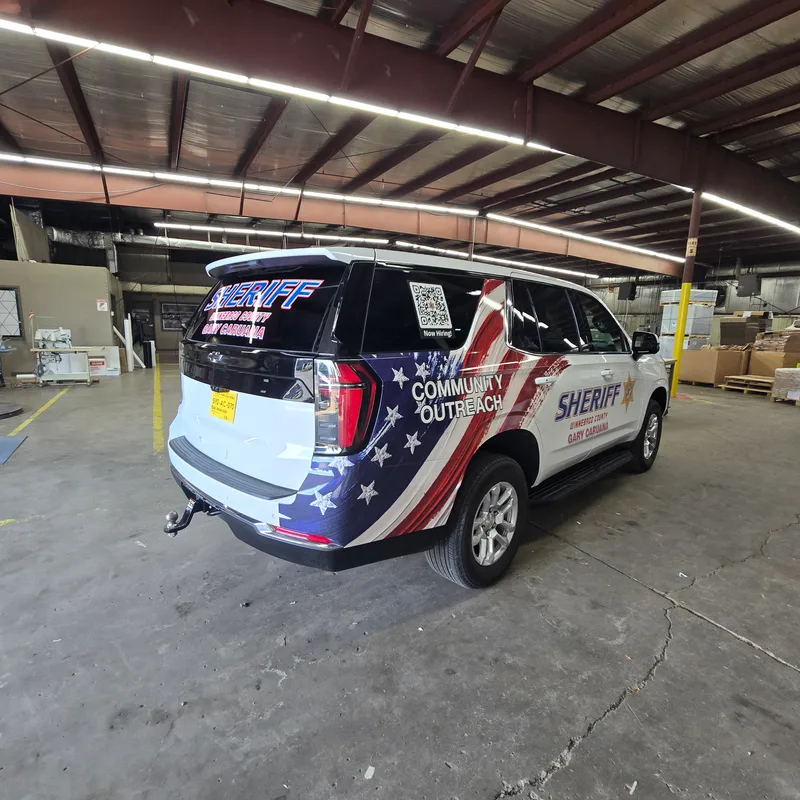 Winnebago County Sheriff Community Outreach Chevy Tahoe — three-quarter rear view showing the American flag treatment across the tailgate and side, 'SHERIFF Winnebago County Gary Caruana' wordmark, and 'COMMUNITY OUTREACH' callout, photographed in the CorPro shop after install.