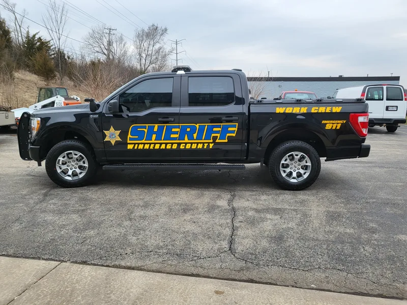 Black Winnebago County Sheriff Ford F-150 with gold-outlined blue "SHERIFF" lettering, star badge and "WORK CREW" callout on the bed.