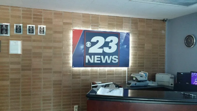 23 News station lobby — backlit "23 NEWS" logo panel with halo lighting on a tan brick wall above the reception desk.